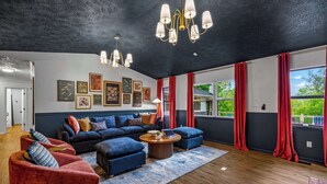 Een moderne woonkamer met een donker plafond, een hoekbank, rode gordijnen en kunstwerken aan de muur.