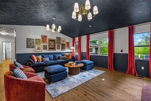 Ein modernes Wohnzimmer mit dunkler Decke, einem Ecksofa, roten Vorhängen und Bildern an den Wänden.