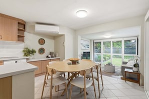A modern kitchen with a dining area, white cabinetry, and a large window with a view of greenery. - Garden Villa at Diggers (Coffs Harbour)