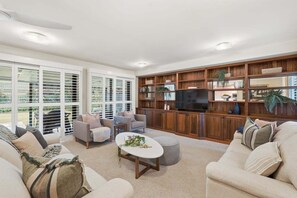 A spacious living room with a large TV, wooden shelving, and comfortable seating. - Garden Villa at Diggers (Coffs Harbour)