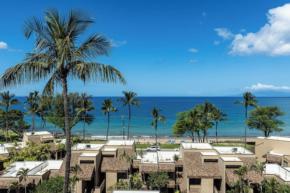 A coastal hotel with multiple-story buildings, a beach view, and palm trees. - Epic Sunsets. Oceanview 2 BR. Walk to Beach and Shops. (Kihei)