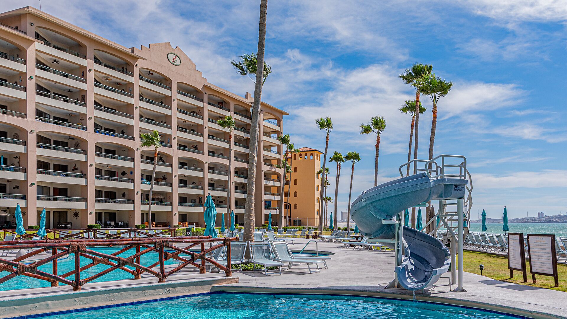 A hotel with a pool, a water slide, and palm trees.