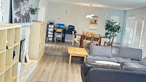 Una sala de estar con sofá, mesa de centro, televisor, chimenea, estanterías y un comedor.
