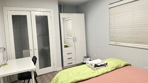 Un dormitorio con cama, escritorio, silla, armario y ventana con persianas.