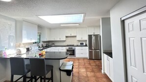 Una cocina moderna con armarios blancos, una isla central con taburetes, microondas, refrigerador y tragaluz.