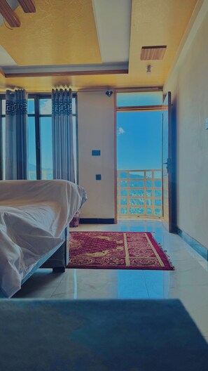 Une chambre d’hôtel avec un lit, un tapis rouge  à motifs, une vue sur le ciel et un balcon.