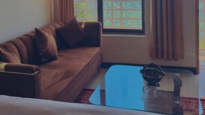Una habitación con sofá, una mesa de centro de vidrio y vistas a montañas a través de una ventana con cortinas.