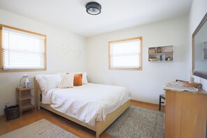 A bedroom with a bed, bedside tables, a dresser, a mirror, and a window with blinds.
