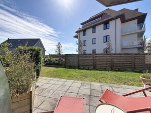 Ein Wohngebäude mit flachem Dach, zahlreichen Fenstern und einem umzäunten Hinterhof mit gepflasterter Terrasse.