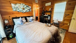 Camera da letto in una baita di legno, con un letto, cuscini, un comodino, una cassettiera, uno specchio e una finestra con persiane.
