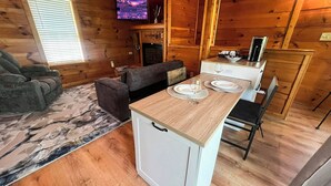 Una cabina accogliente con divano, un piccolo tavolo da pranzo con piatti, televisore e camino.