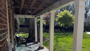 A covered patio with stone flooring, a glass table, metal chairs, and a brick wall. - Richmond Near West End, Charming Private Cottage (Richmond)