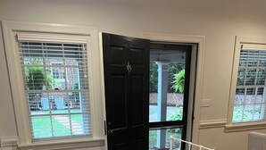 A bedroom with a bed, white bedding, a black door, and a view of a garden through a window. - Richmond Near West End, Charming Private Cottage (Richmond)