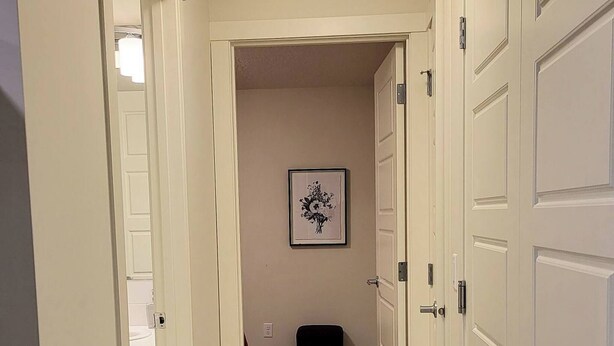 A hallway with white doors, a framed picture on the wall, and a fluffy rug on the floor. - The Waterview at Rockland (Calgary)