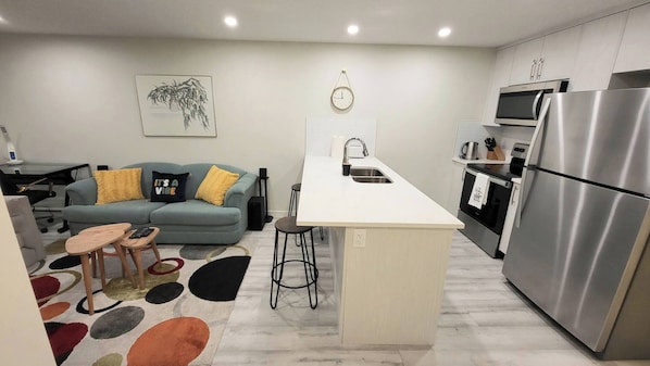 A modern kitchen with a central island, stainless steel appliances, and a grey sofa with yellow cushions.