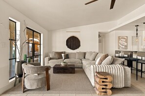 A modern living room with a sectional sofa, a coffee table, and a dining area with bar stools. - INTRVL Wellness House: Stargazing, Fire Pit & Desert Views (Joshua Tree)