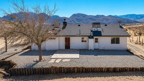 Una casa de un solo piso con entrada de grava, cerca de madera y montañas al fondo.