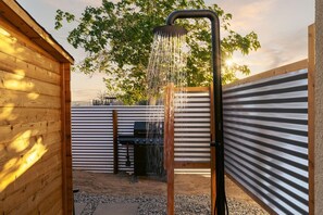 A wooden outdoor shower with a metal frame, surrounded by a wooden fence and a metal wall. - INTRVL Wellness House: Stargazing, Fire Pit & Desert Views (Joshua Tree)