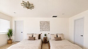 Un dormitorio con dos camas, un tapete de diseño geométrico, una lámpara de pared y una planta en maceta.