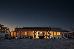A modern house with a covered patio area, outdoor seating, and a gravel driveway. - INTRVL Wellness House: Stargazing, Fire Pit & Desert Views (Joshua Tree)