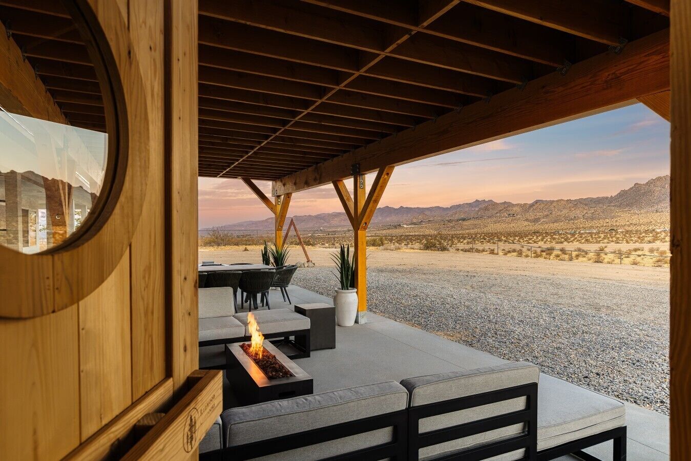 An outdoor seating area with a fire feature, a round mirror, and a view of a desert landscape.