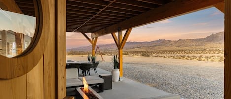 An outdoor seating area with a fire feature, a round mirror, and a view of a desert landscape.