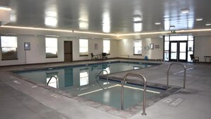 Une piscine intérieure à l’eau claire, dotée d’échelles en métal et d’un sol carrelé.