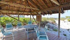 Una terraza de madera con techo de paja, mobiliario exterior y vista a la playa.
