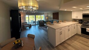 Una cocina moderna con una isla central, un comedor con mesa y sillas, y una sala de estar con sofá y mesa de centro.