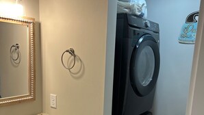 A compact laundry area with a washing machine, a sink with granite countertop, and a mirror with a decorative frame.