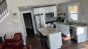 A modern kitchen with white cabinets, a granite countertop, stainless steel appliances, and a dining area with a red leather couch.