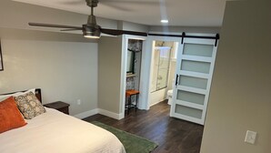A bedroom with a bed, a ceiling fan, a green rug, and a bathroom with a shower and toilet.