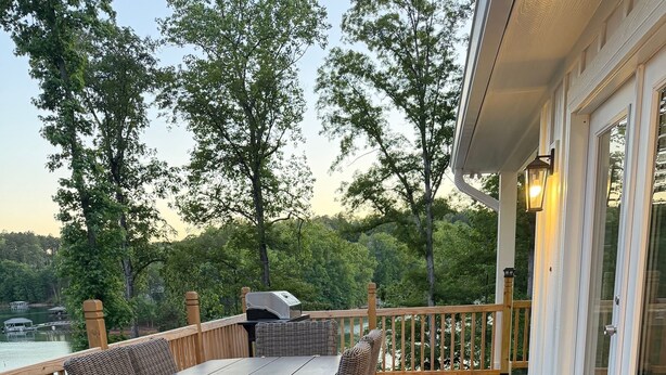 A wooden deck with wicker furniture, a grill, and a view of a lake.