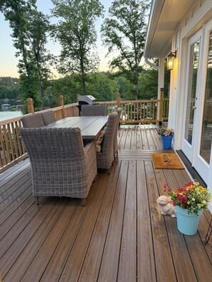 A wooden deck with wicker furniture, a grill, and a view of a lake.