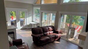 A spacious living room with a leather sofa, a dining area, and a balcony with a view of a lake.