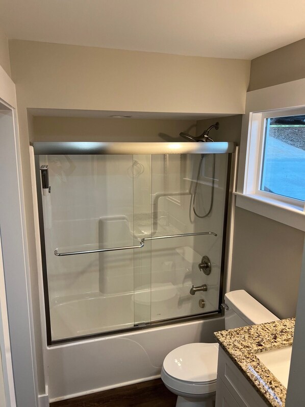 A bathroom with a glass-enclosed shower, a toilet, and a granite countertop.