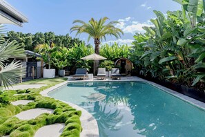 Ein Swimmingpool mit Liegestühlen, einer Palme und üppiger Bepflanzung.