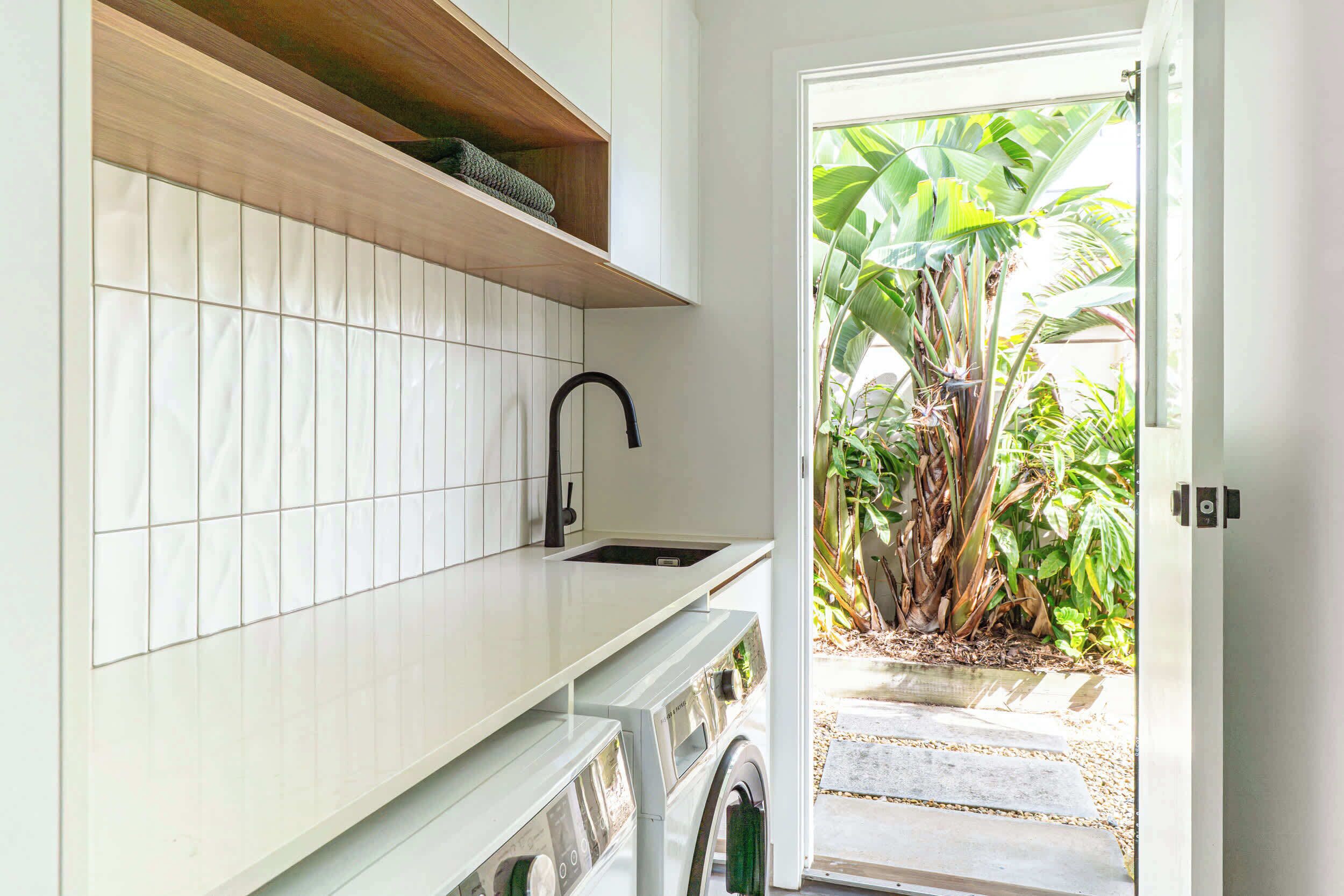 Una cucina moderna con lavatrice integrata, un lavandino e una mensola in legno.