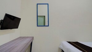 A room with a bed, a small table, a wall-mounted TV, and a mirror. - Lotus Inn (Pekanbaru)