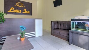 A reception area with a sign reading 'Lotus Inn,' a leather sofa, a fish tank, and a potted plant. - Lotus Inn (Pekanbaru)