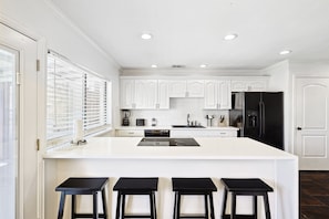 A modern kitchen with white cabinetry, a black refrigerator, and a central island with stools.