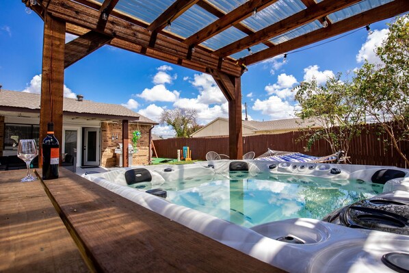 Un jacuzzi bajo una pérgola de madera con cielo despejado.