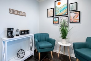 A room with teal armchairs, a coffee station, and wall art.