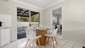 Une cuisine compacte avec un coin repas, comprenant une table ronde en bois avec des chaises, un four encastré et un lave-linge.