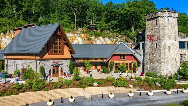 Eine rustikale Lodge mit einem steinernen Turm, der 'Ruby Falls' beschriftet, ein Holzbau mit geneigtem Dach und einladende Schilder.