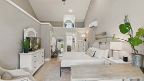 Quarto com cama, mesas de cabeceira, cômoda, televisão e planta em vaso.