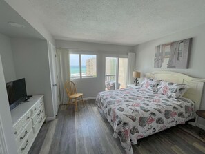 Ein Schlafzimmer mit Bett, Sessel, Fernseher und Meerblick durch ein Fenster.