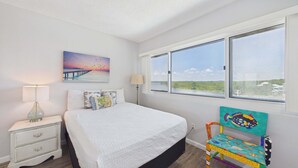 Un dormitorio con cama, mesita de noche, lámpara, cuadro, ventana y una silla.