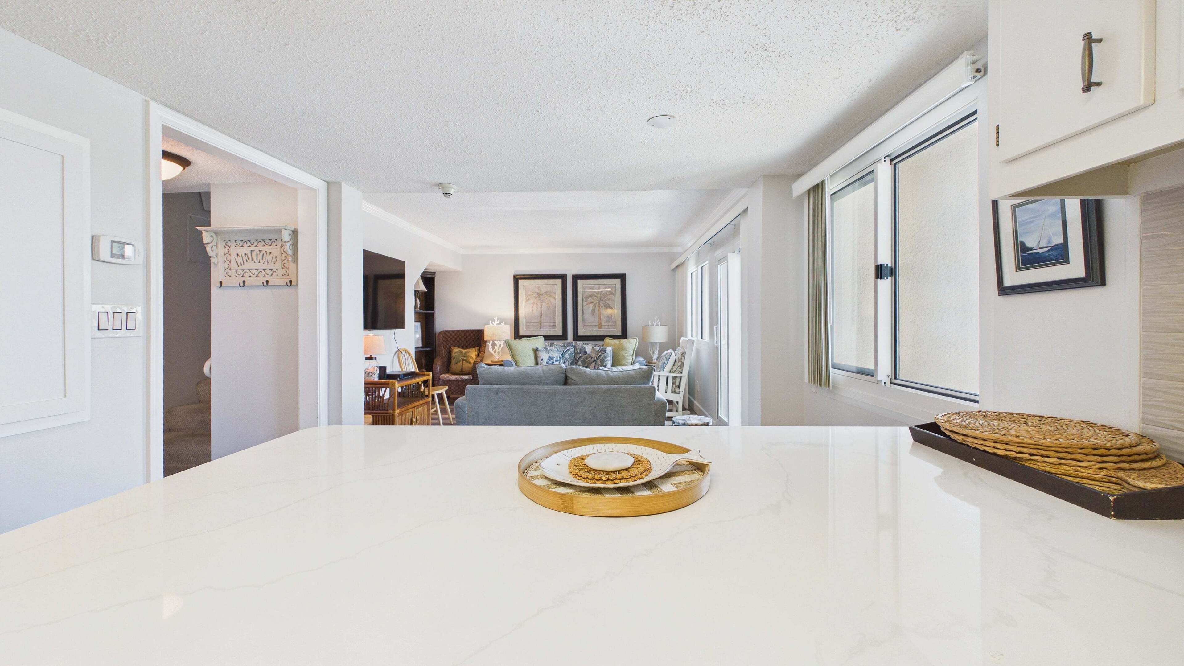 A modern living room with a white marble coffee table, a grey sofa, and a dining area with wooden furniture.