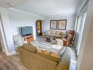 Ein Wohnzimmer mit Fernseher, Sofa, Sessel und Wanddekoration.